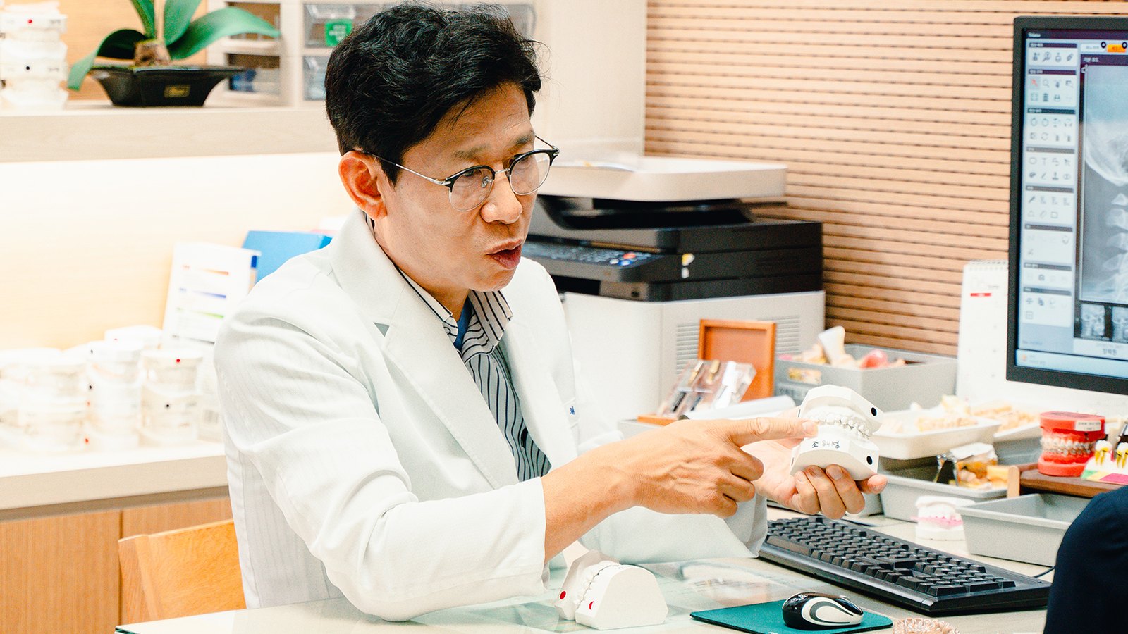 치과의사가 진료실에서 치아 모형을 들고 손으로 가리키며 설명하는 모습